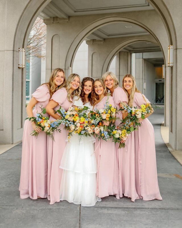 Bride wearing a flowy wedding dress poses with her bridesmaids wearing pink