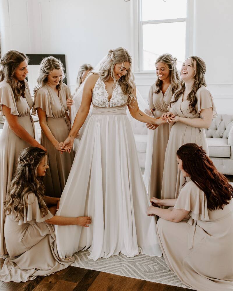 Bride laughing and smiling with her bridesmaids as they help her get ready