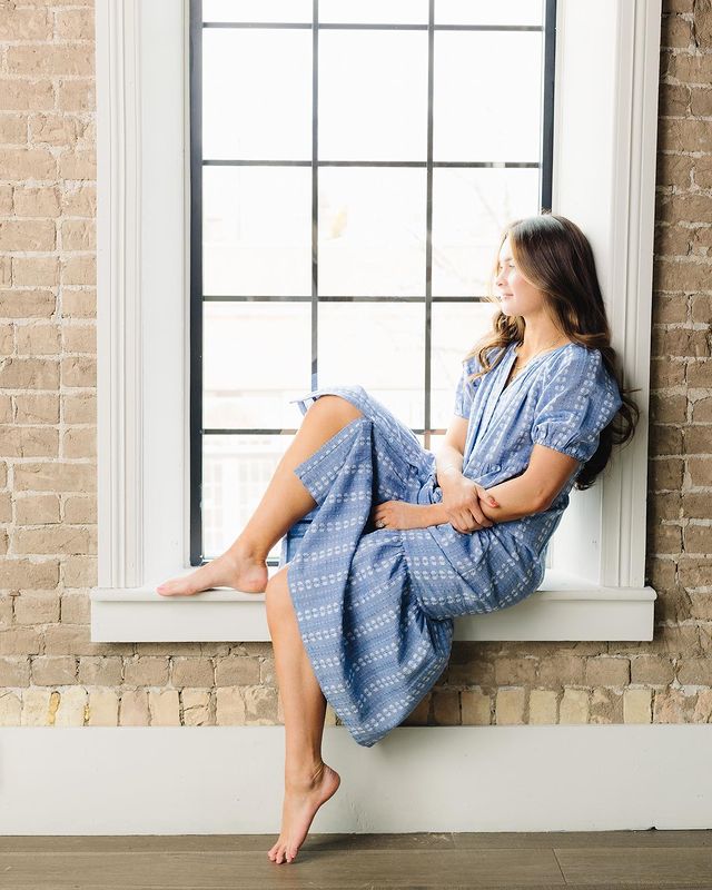 A woman sitting in a window wearing a summer Called to Surf dress